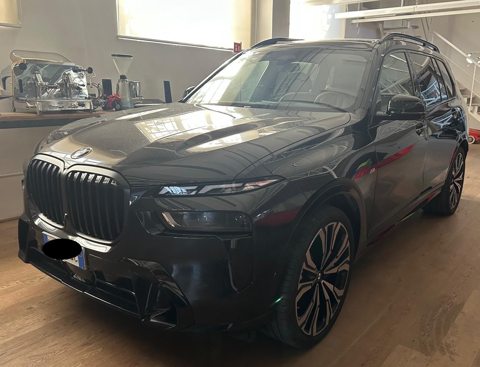 Un SUV BMW X7 nero parcheggiato all'interno su un pavimento di legno, visto dal lato anteriore del passeggero.