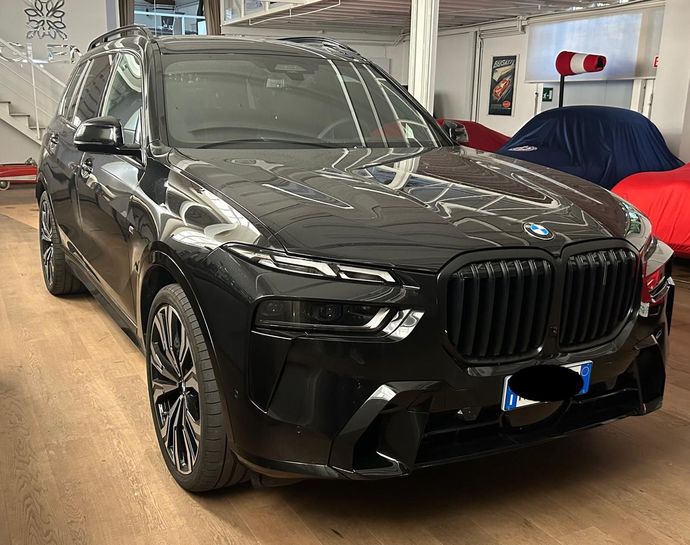Un SUV BMW nero parcheggiato all'interno di uno showroom con pavimento in legno e auto coperte sullo sfondo.