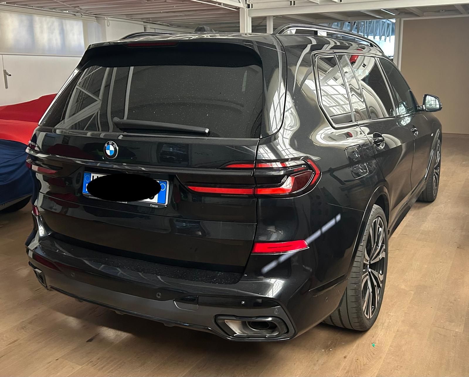 Una BMW X7 SUV nera parcheggiata al chiuso, vista da dietro, che mostra i fanali posteriori, i terminali di scarico e i cerchi in lega.