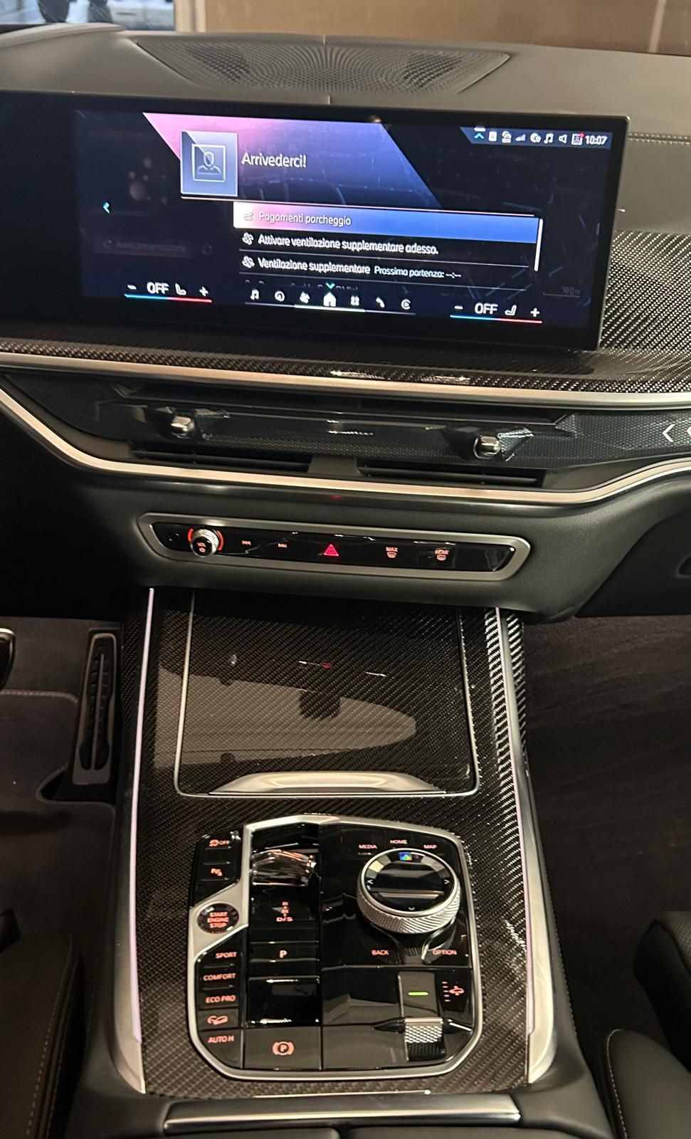 Cruscotto moderno per auto, caratterizzato da un ampio schermo per l'infotainment, finiture in fibra di carbonio e selettore del cambio sulla console centrale.