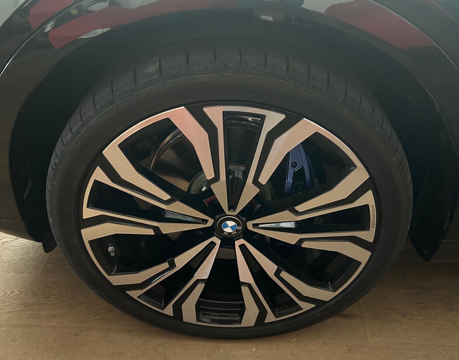 Primo piano di un cerchio in lega BMW nero e argento con pinza freno blu, su uno sfondo nero.