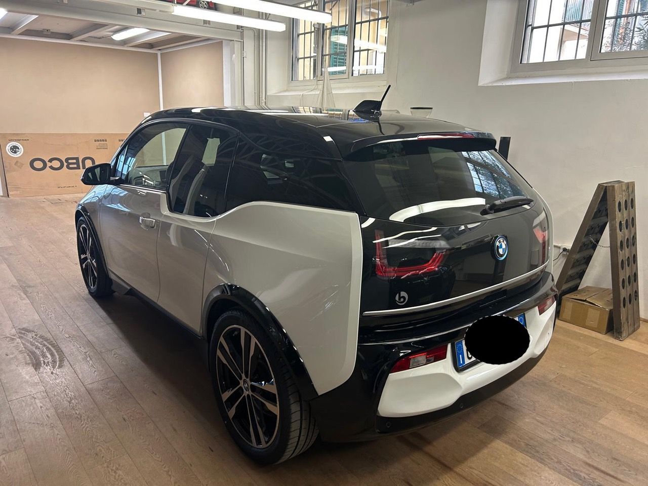 Una BMW i3 bicolore bianca e nera parcheggiata all'interno di un'officina con pavimento in legno.