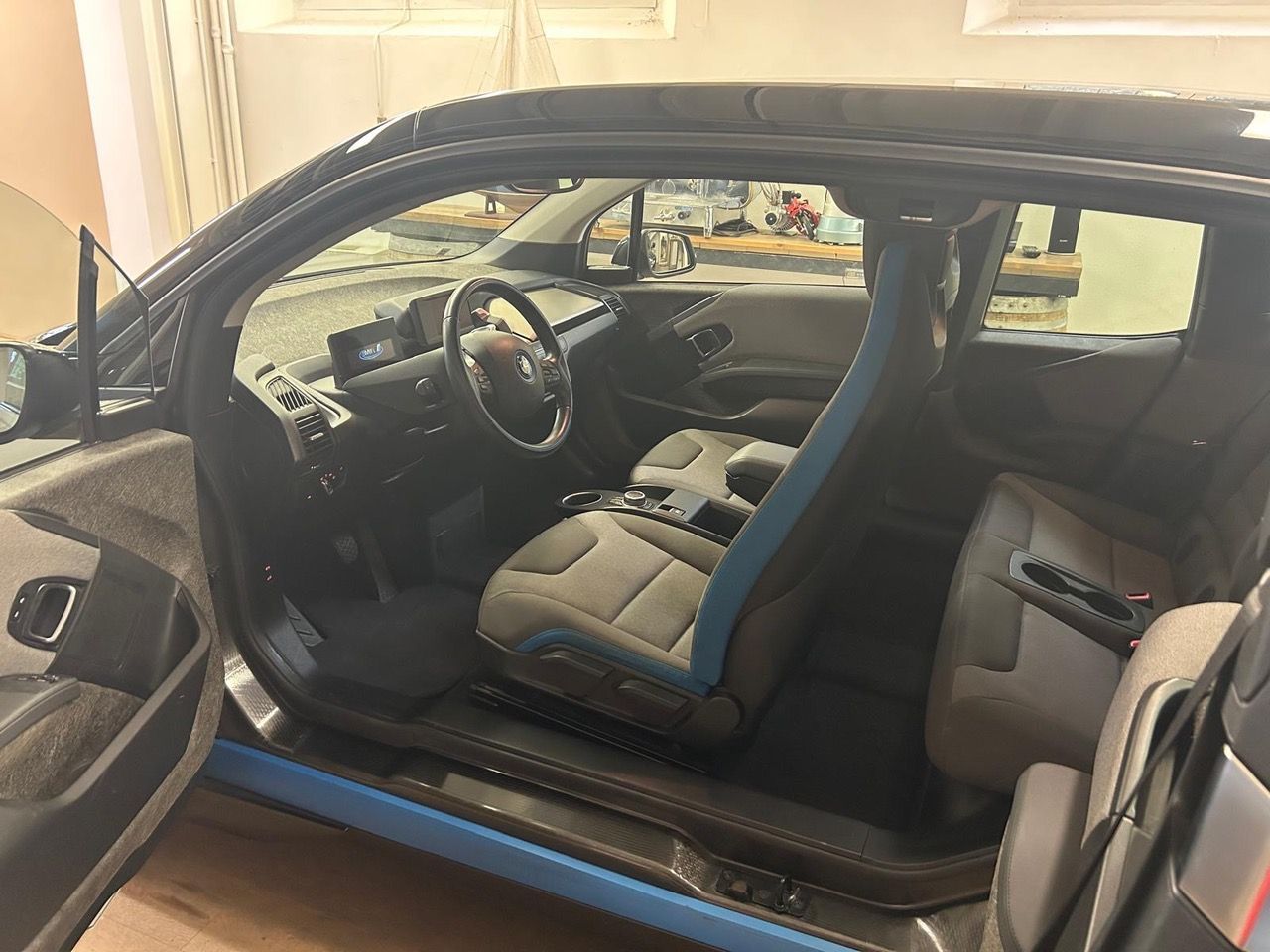 L'interno di un'auto con sedili grigio chiaro, inserti blu, volante e cruscotto digitale.