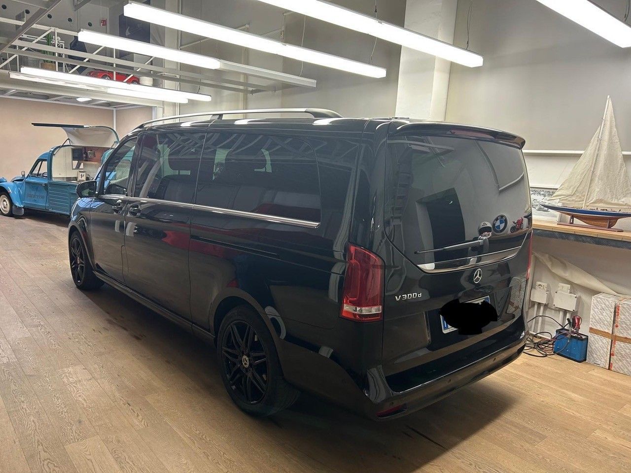 Un furgone Mercedes-Benz Classe V nero parcheggiato all'interno di un'officina, con un modellino di barca sullo sfondo.