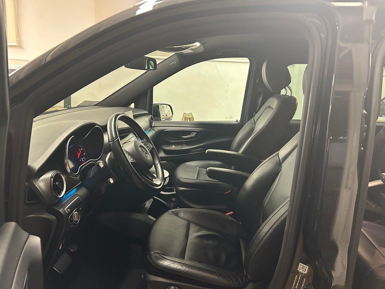 Vista interna di un veicolo nero che mostra il sedile del conducente, i rivestimenti in pelle, il volante e il cruscotto.