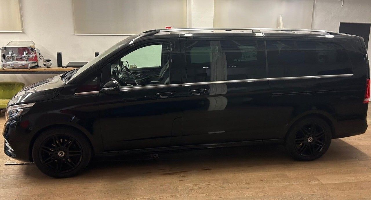 Un minivan nero parcheggiato all'interno su un pavimento di legno, visto di profilo.