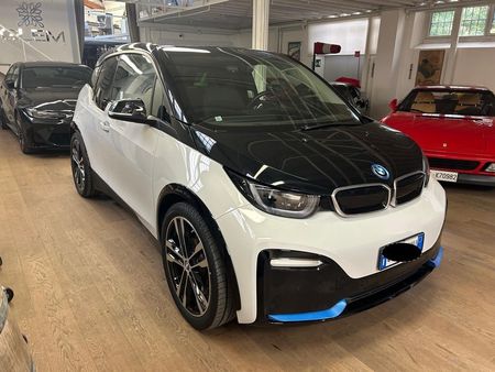 Una BMW i3 elettrica bicolore bianca e nera parcheggiata all'interno di uno showroom, con un'auto rossa e un'auto nera sullo sfondo.