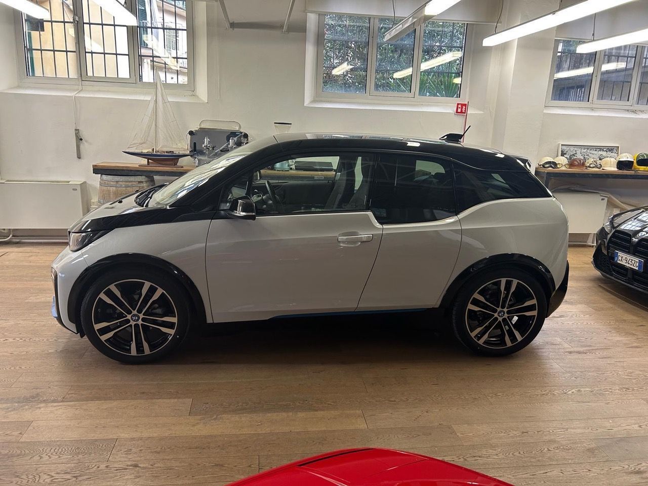 Vista laterale di una BMW i3 bianca con tetto nero parcheggiata all'interno di uno studio o showroom luminoso in stile industriale.