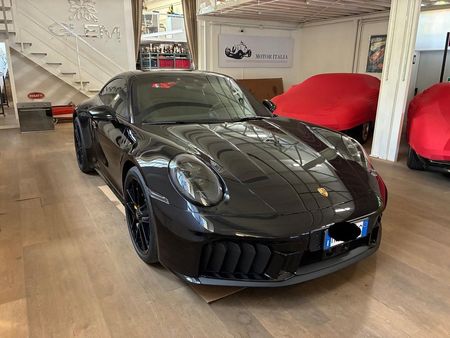 Auto sportiva nera in uno showroom, con auto coperte di rosso sullo sfondo.