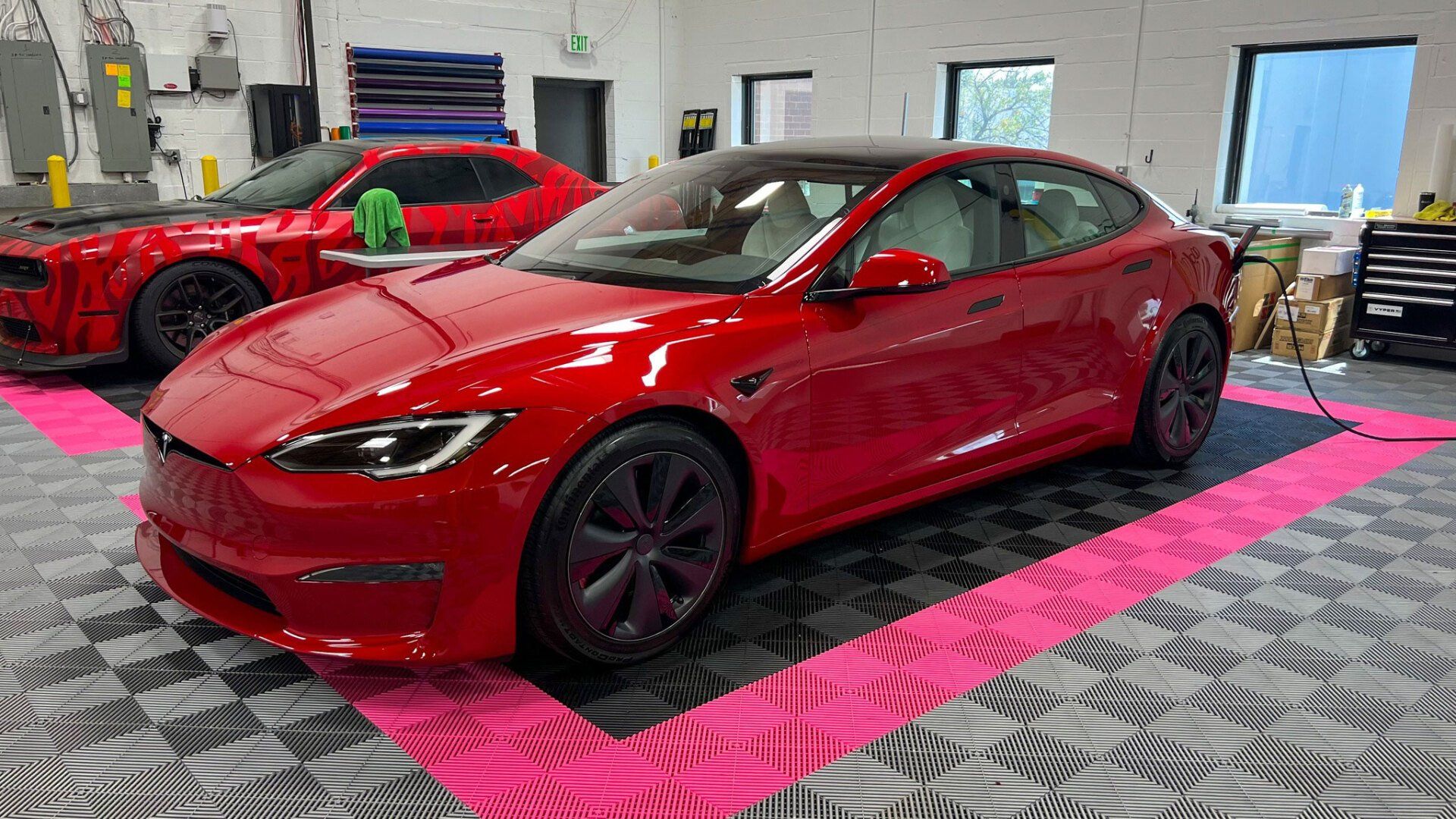 A red tesla model s is parked in a garage next to another red car.