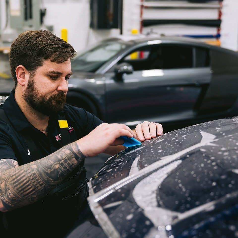 Technician installing paint protection film on a vehicle hood.