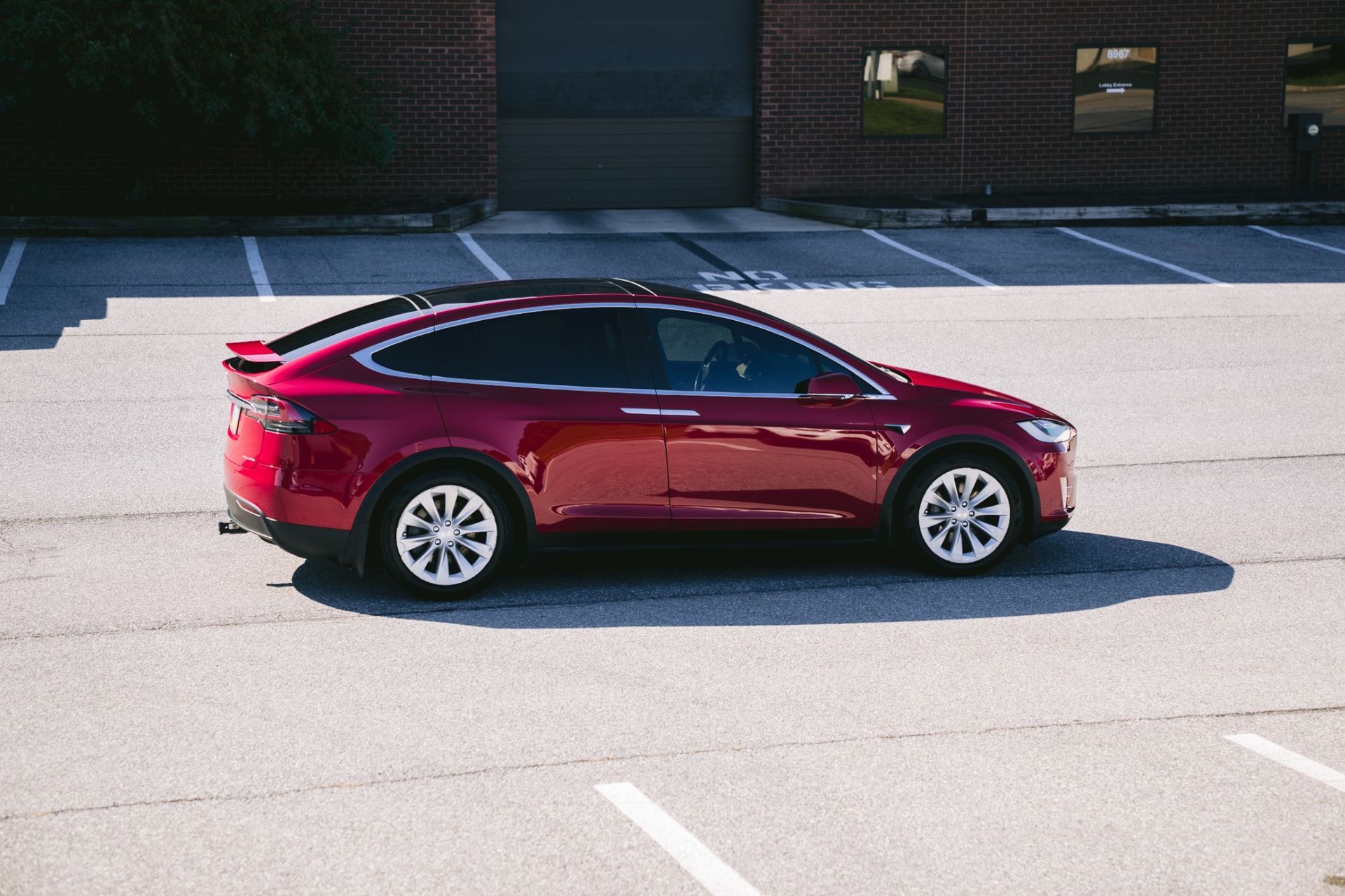 Red Tesla sedan parked in a sunny lot, side view