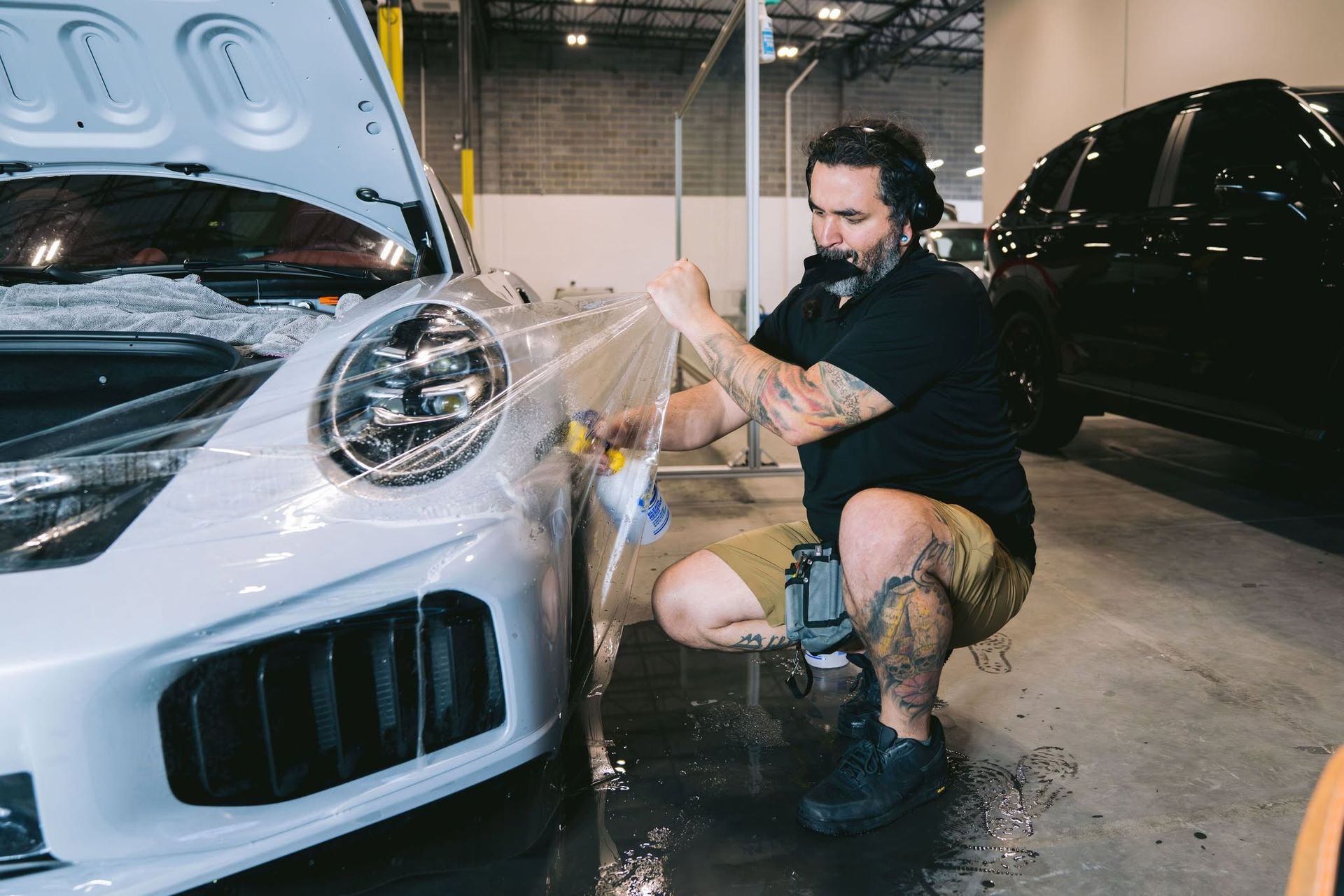 Professional technician applying clear ppf to the front fender of a white sports car