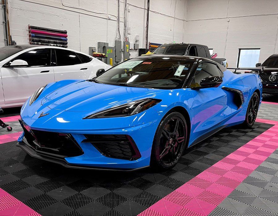 A blue sports car is parked on a checkered floor in a garage.