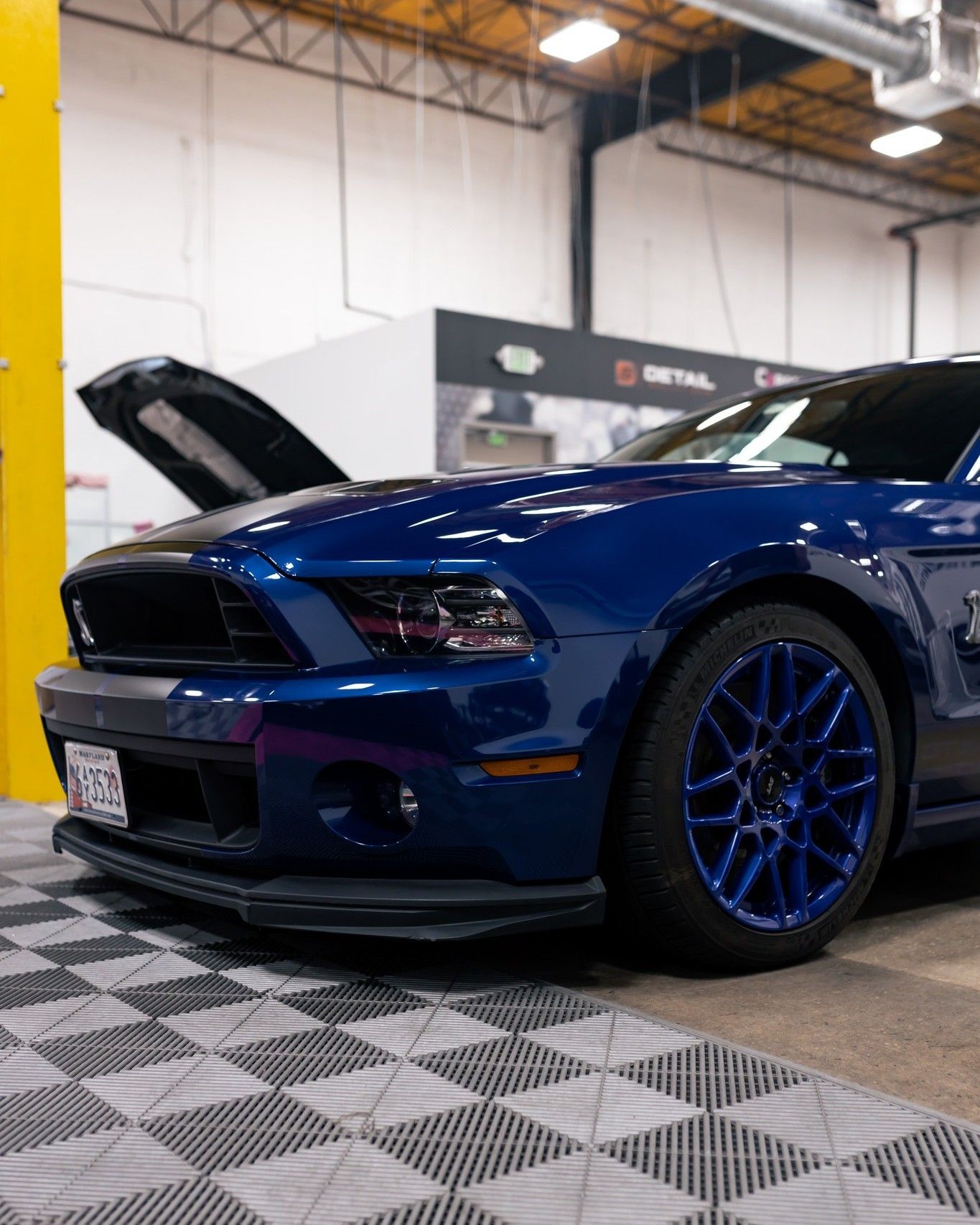 A blue mustang is parked in a garage with its hood up.