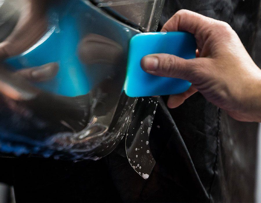 A person is using a blue sponge to apply a film to a car.