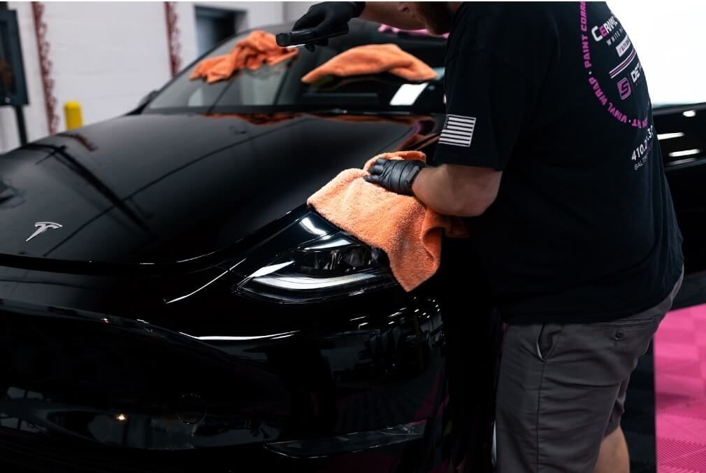 A man is cleaning a black tesla model 3 with a towel.