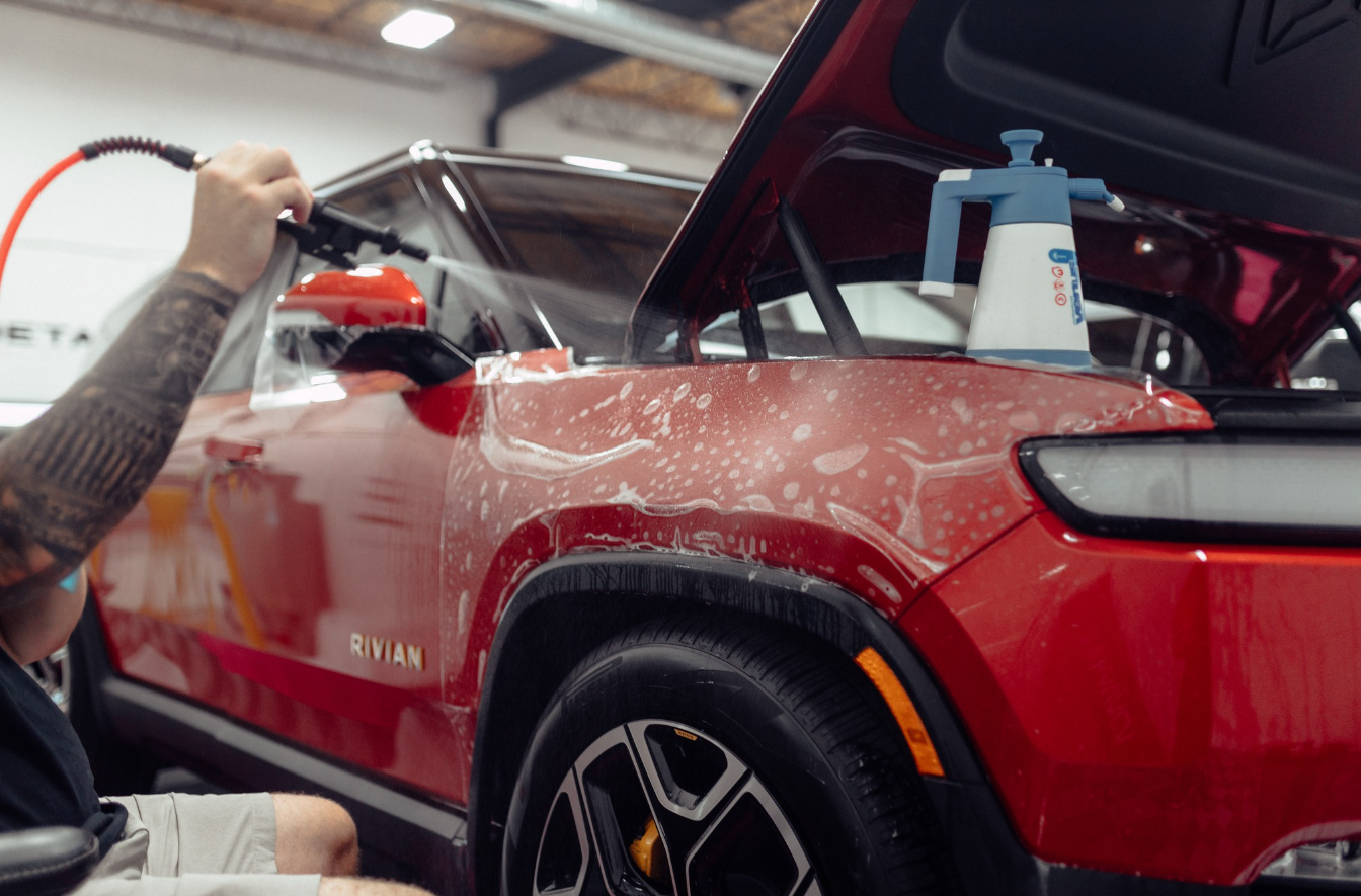 A man is cleaning a red car with a spray bottle.