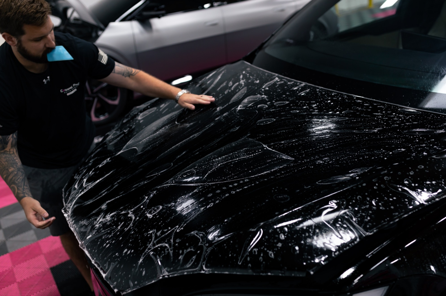 A man is covering the hood of a black car with plastic wrap.