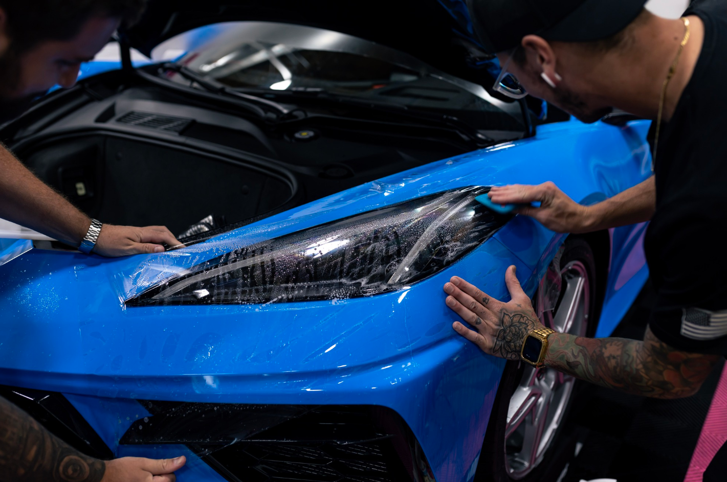 Two men are wrapping a blue car with a protective film.