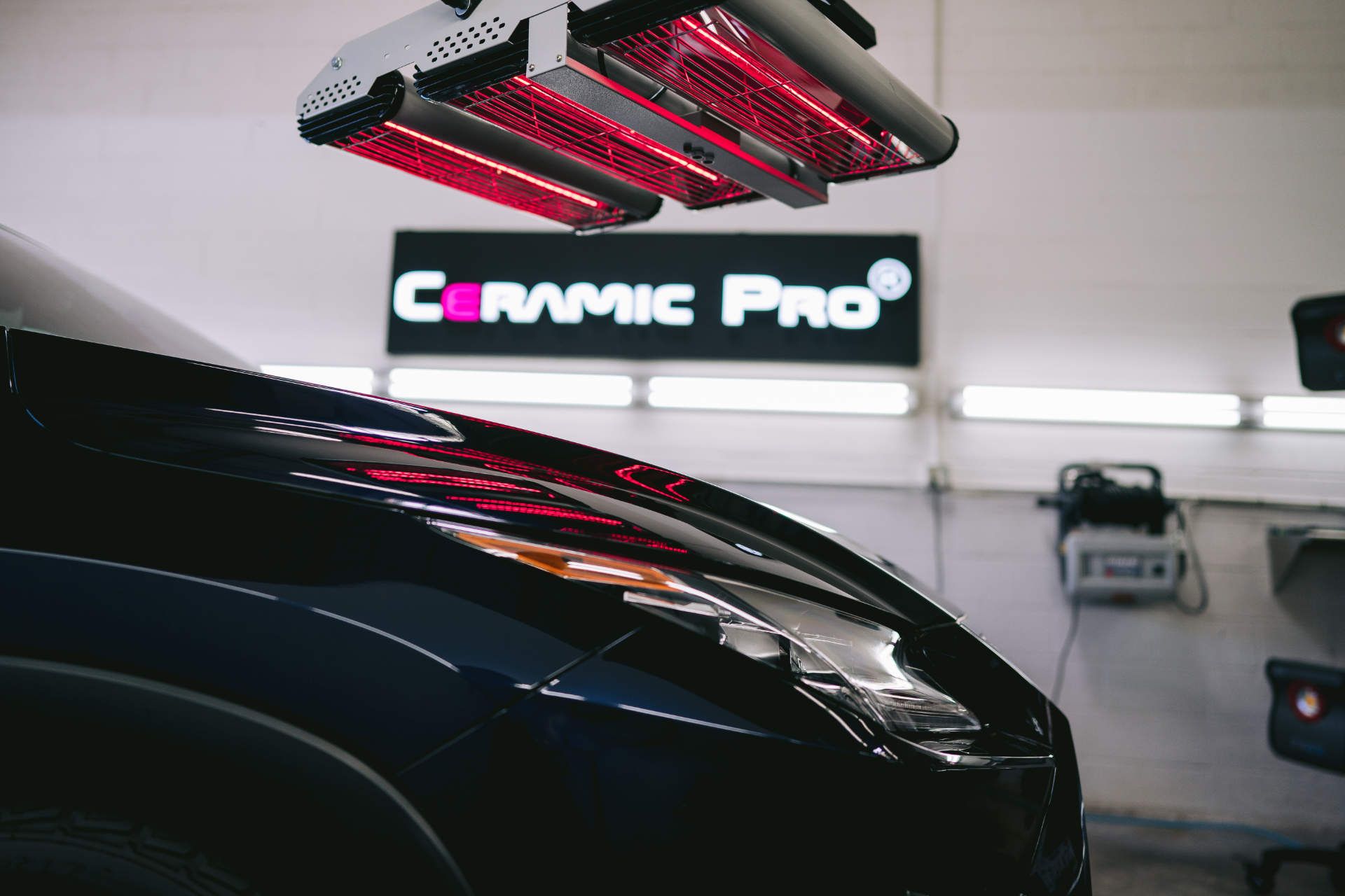 A car is sitting under a red light in a garage.