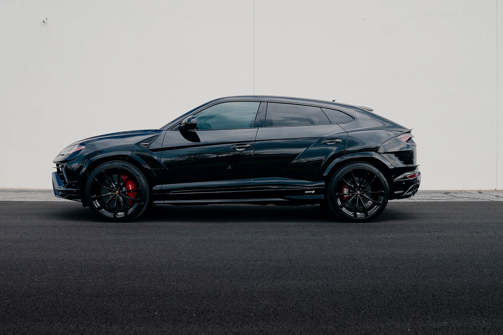 A black lamborghini urus is parked on the side of the road.