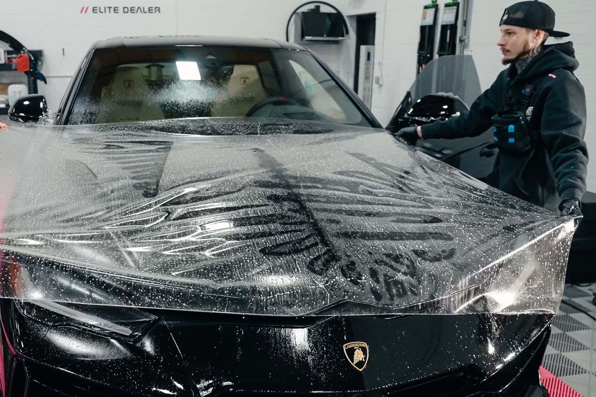 A man is wrapping a black car with a clear plastic covering.