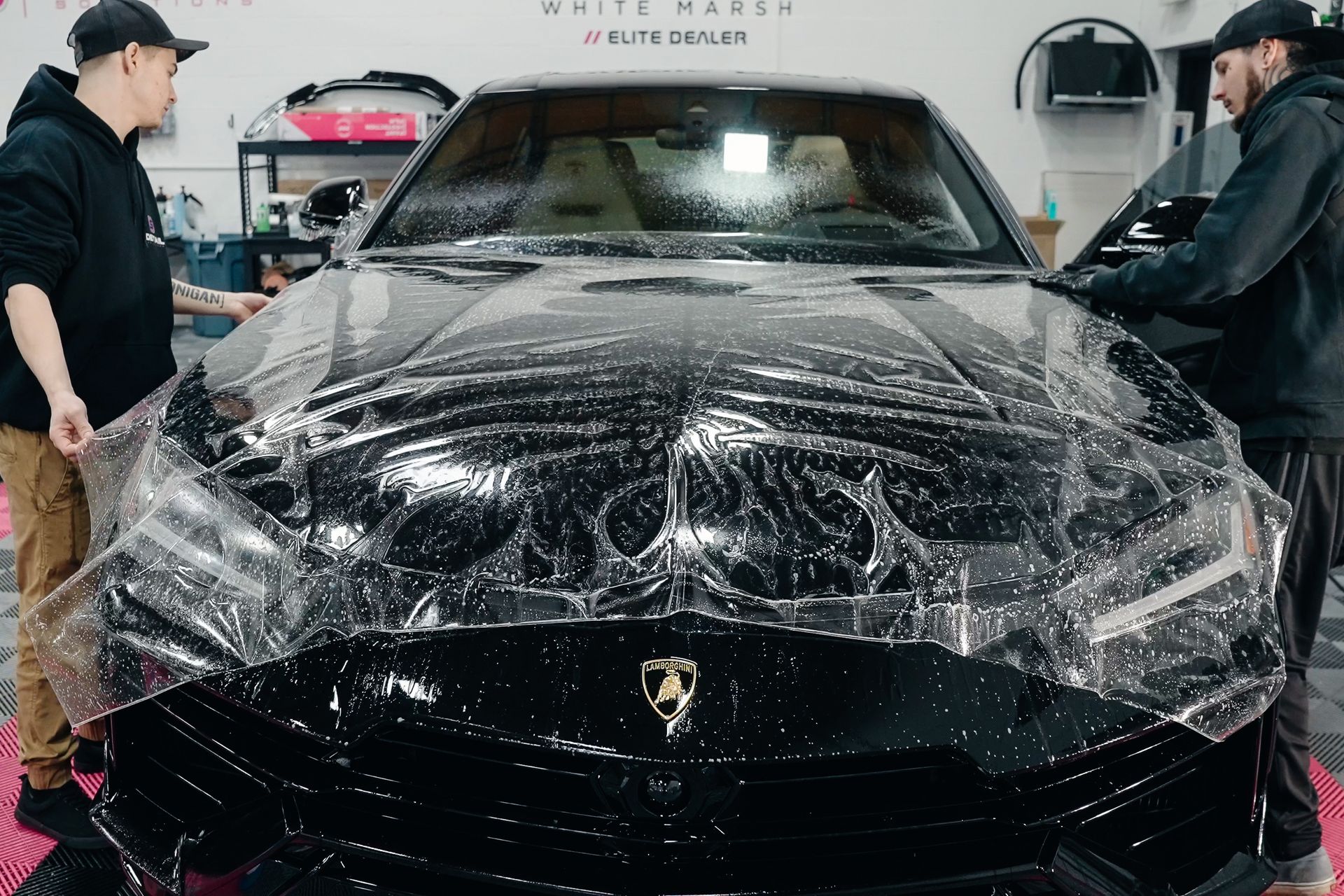 Two men are wrapping a black car with clear plastic.