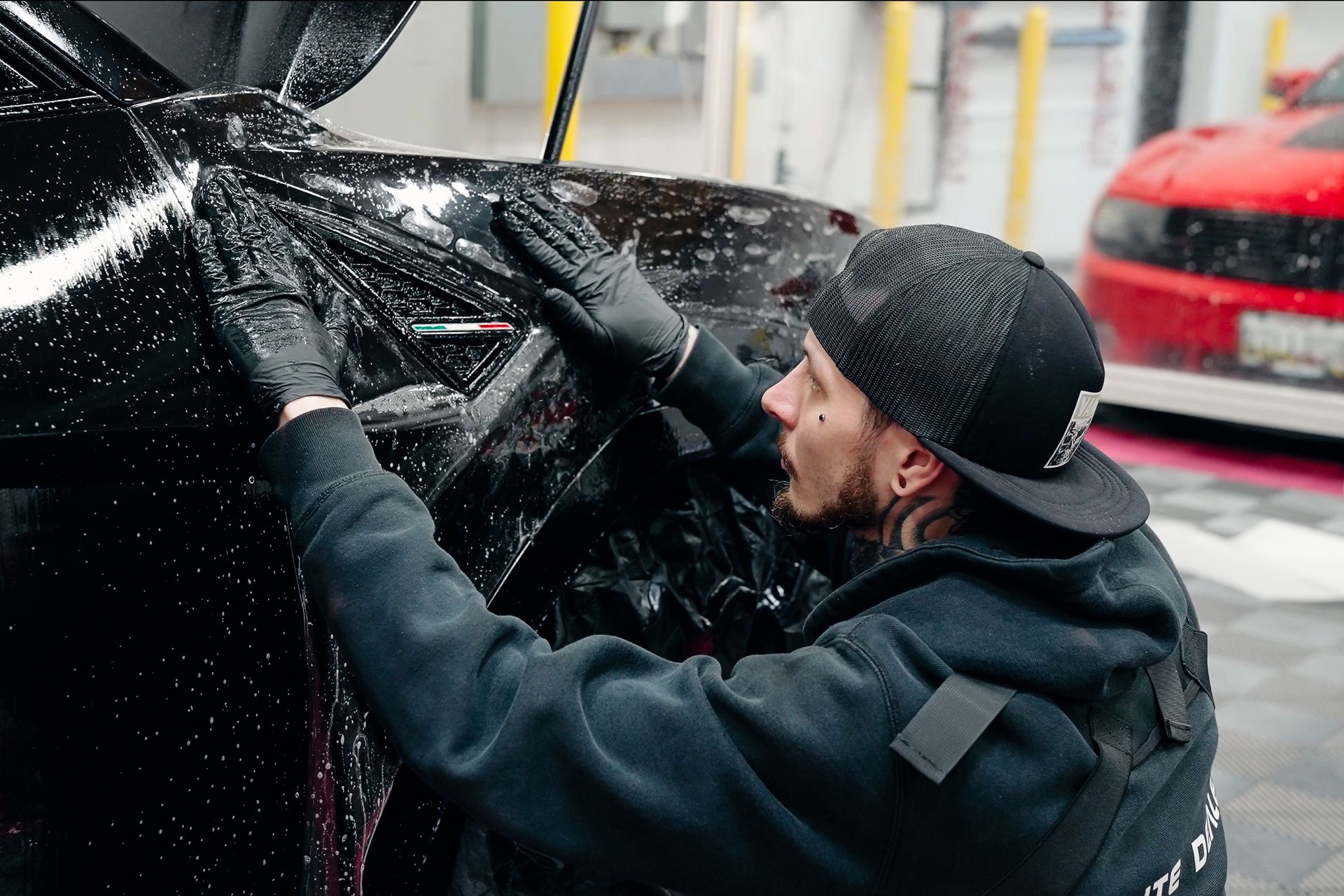 A man in a hat and gloves is wrapping a black car.