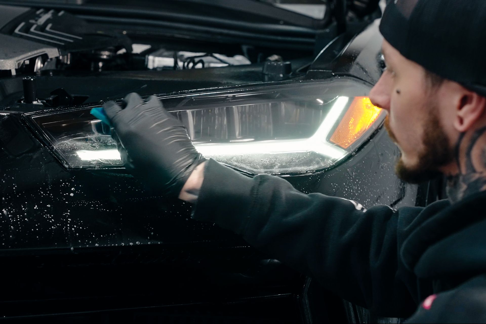 A man is cleaning the headlights of a car.