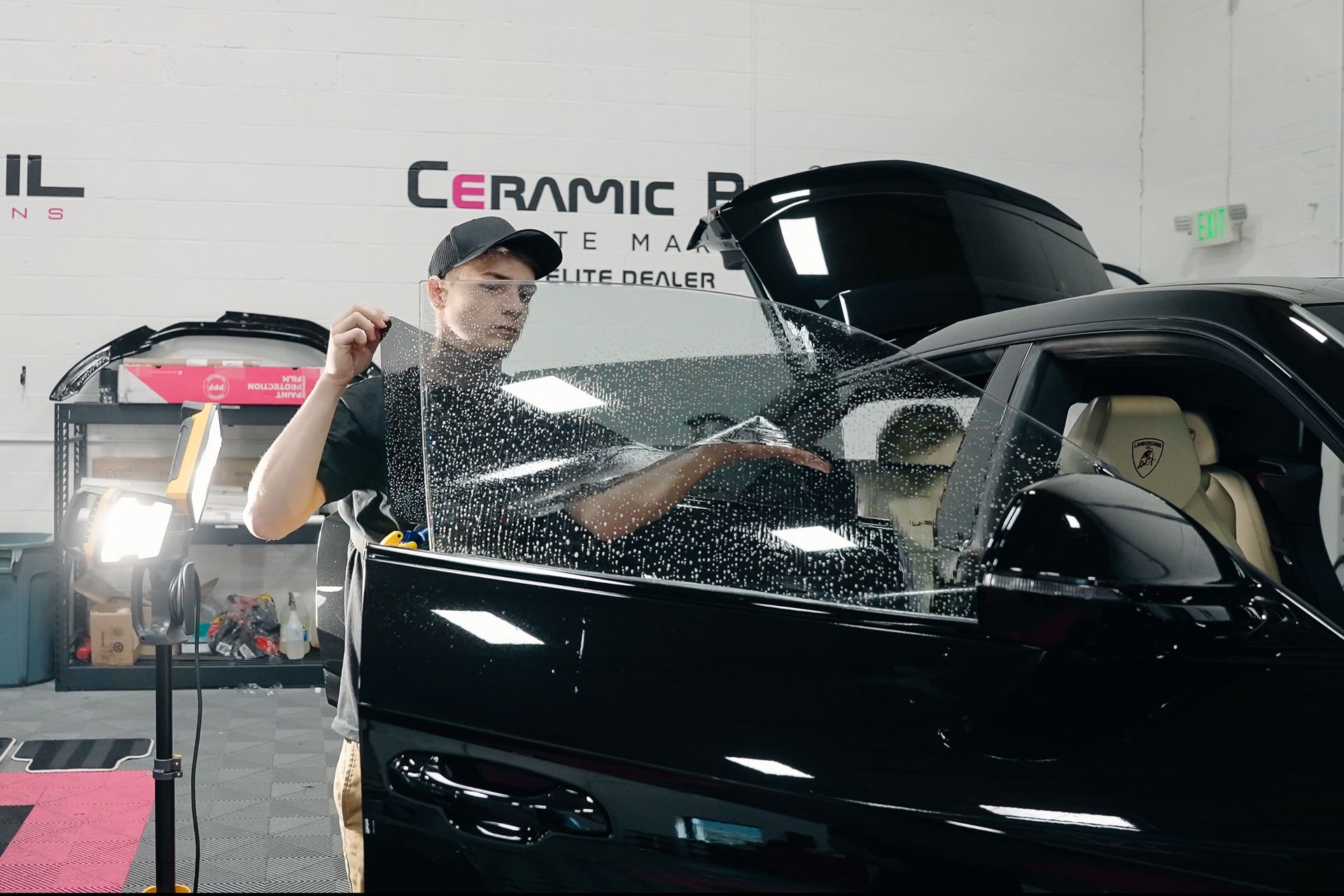 A man is applying window tinting to a black car.
