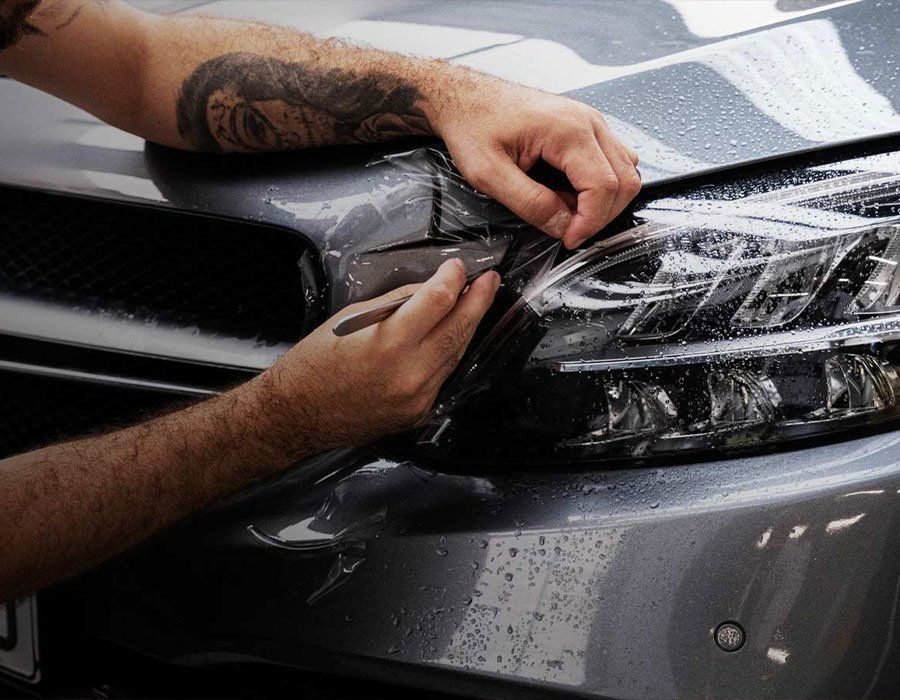 A man is applying a protective film to the headlight of a car.