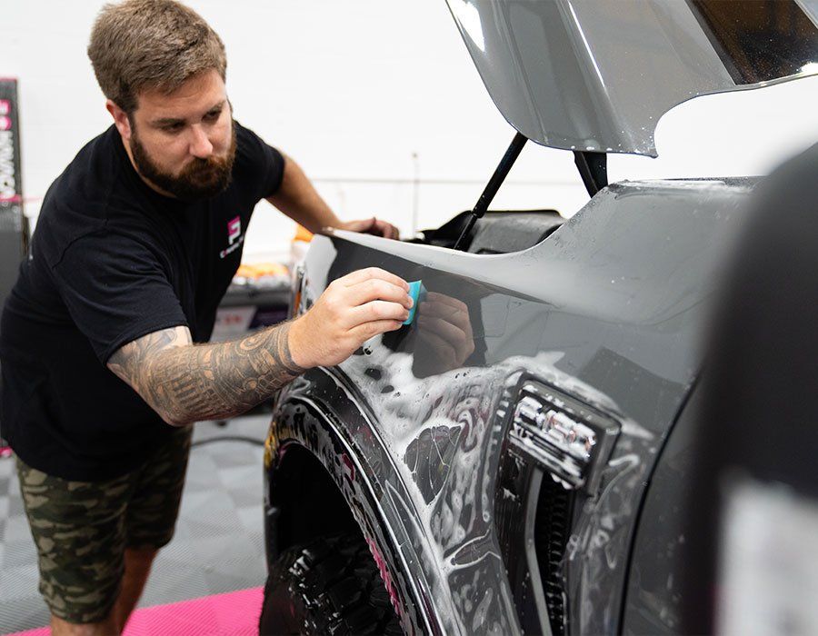 A man is wrapping a car with plastic wrap in a garage.