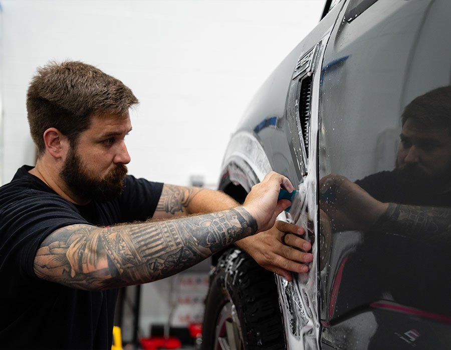 A man with tattoos is wrapping a car with plastic wrap.