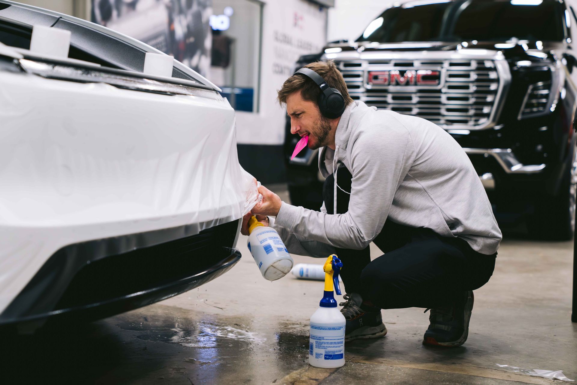 Person applying protective film to a black car's hood. Pink tool, bubbles visible, indoors.
