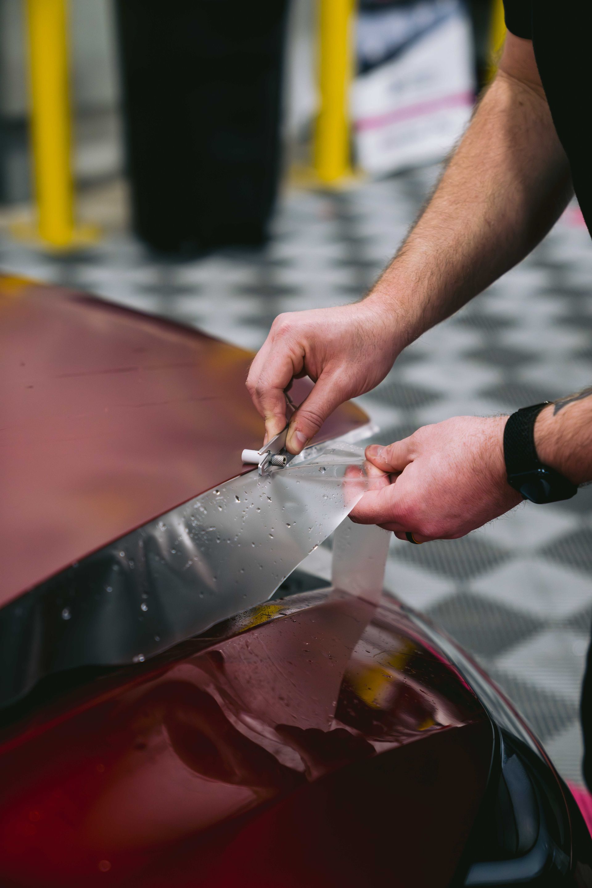 Hands trimming PPF on a red car during professional installation.
