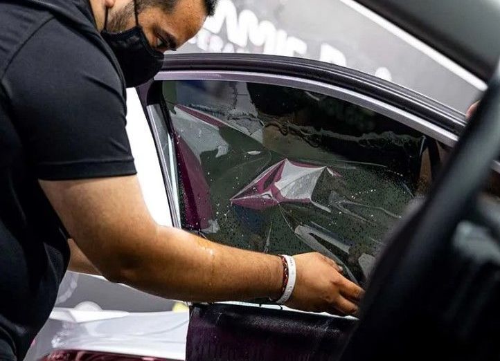 A man wearing a mask is installing window tinting on a car.