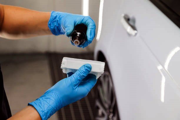 a person wearing blue gloves is holding a bottle in front of a white car .