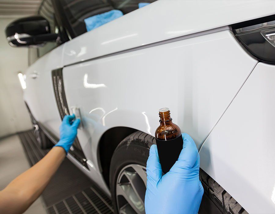 A person is applying a coating to a white car.