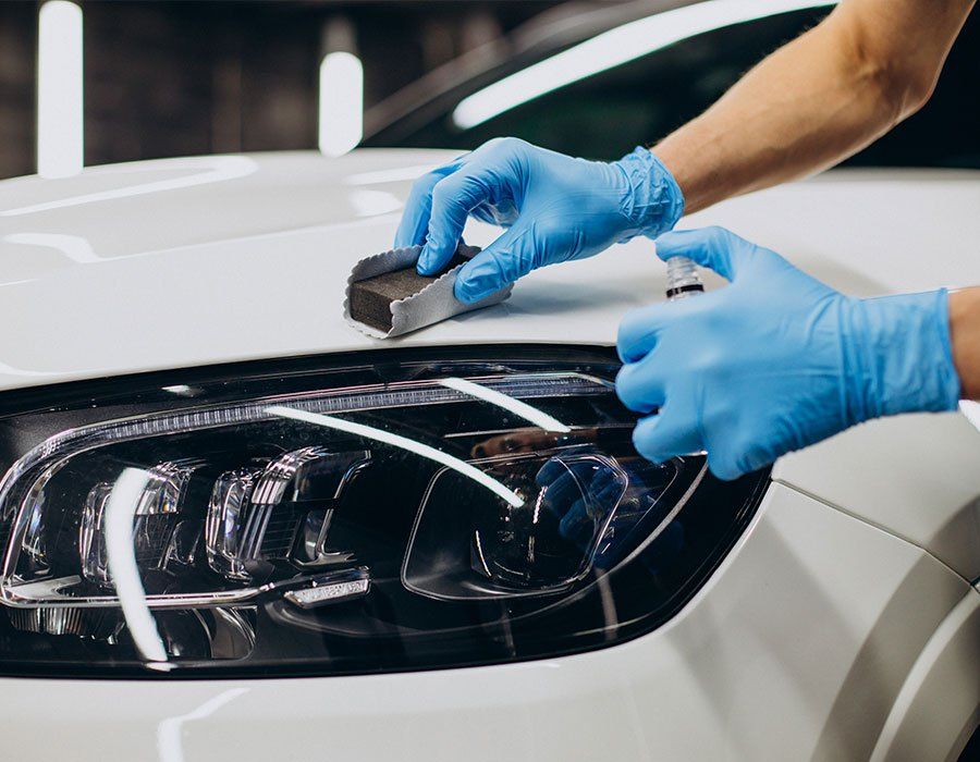 A person wearing blue gloves is polishing the headlight of a white car.