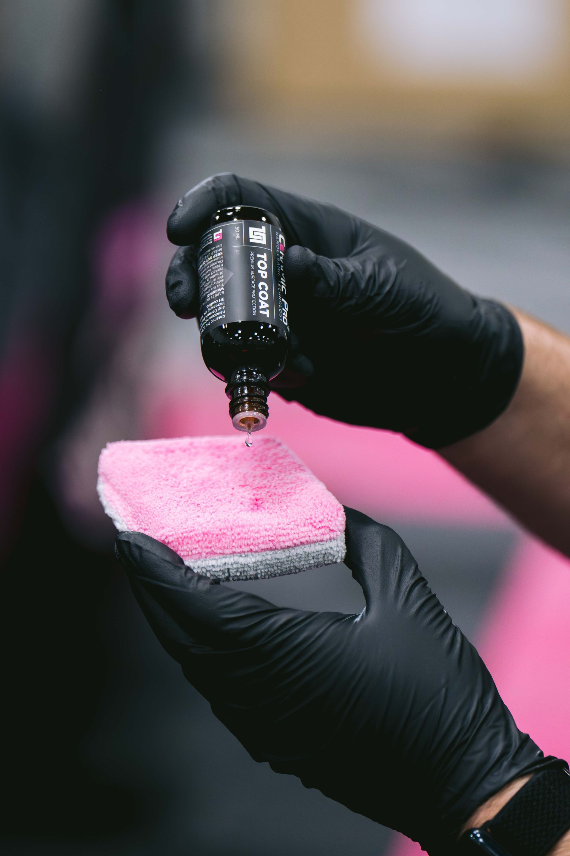 Hands in black gloves applying liquid from a small bottle onto a pink applicator pad.