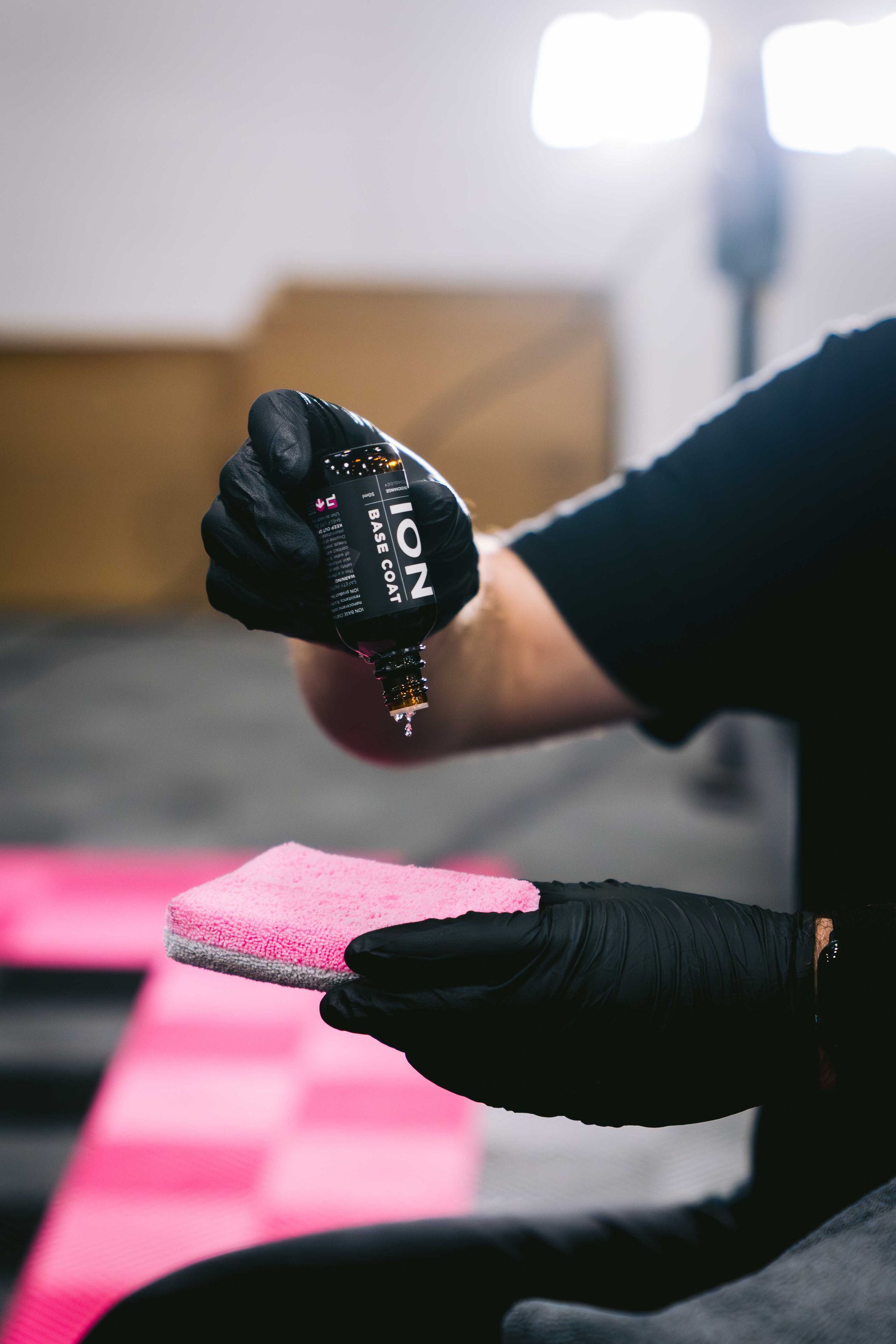 Gloved hand holding ceramic coating bottle over pink applicator pad.