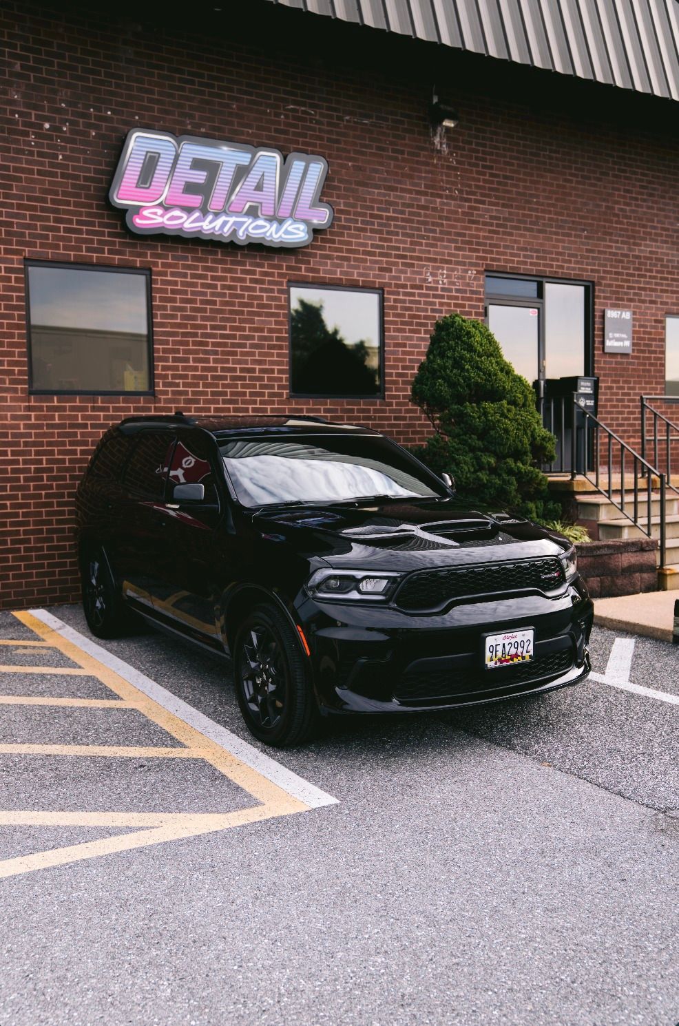 Black SUV parked outside a brick detail shop with a neon sign and wet pavement
