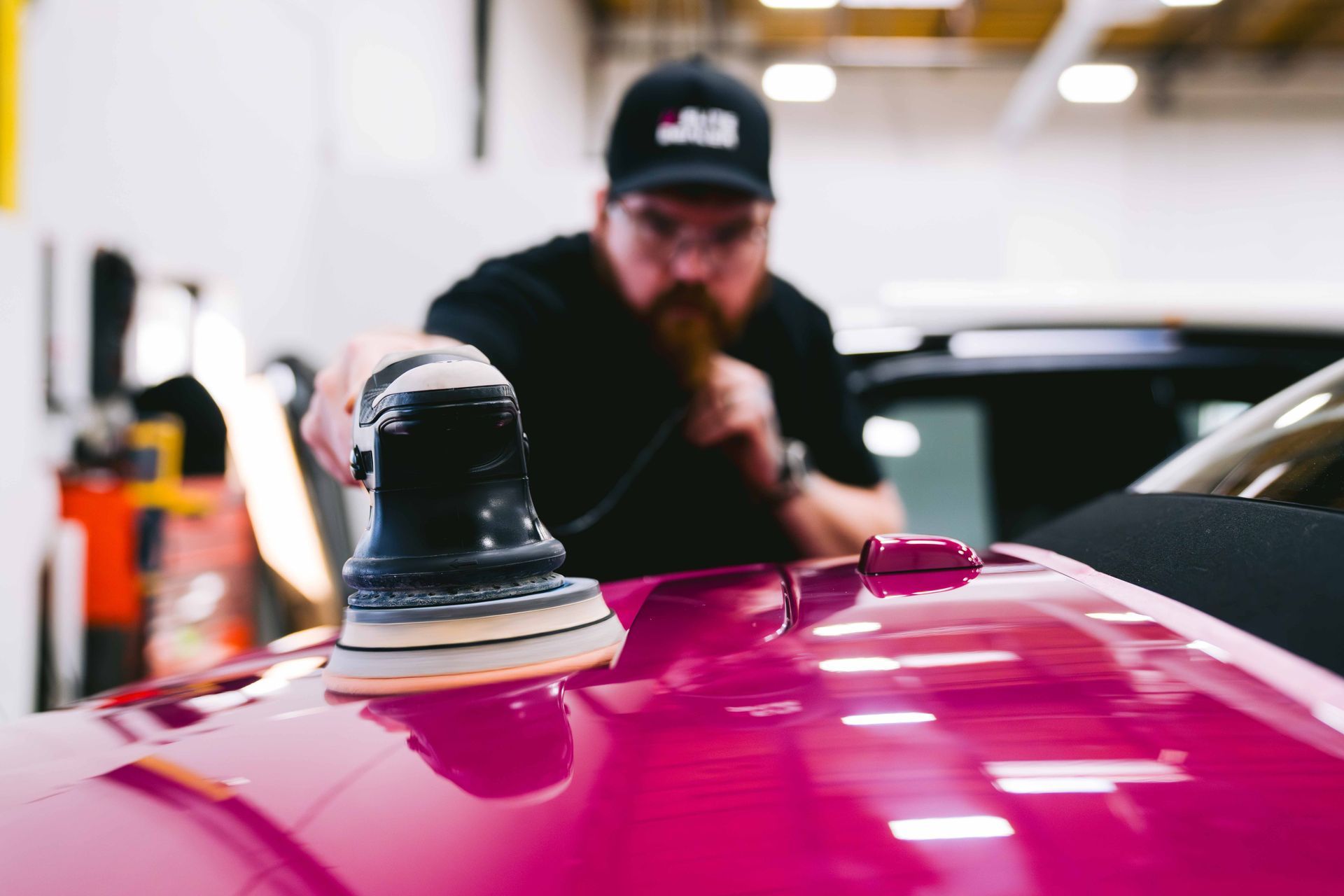 A man is polishing the hood of a pink car.