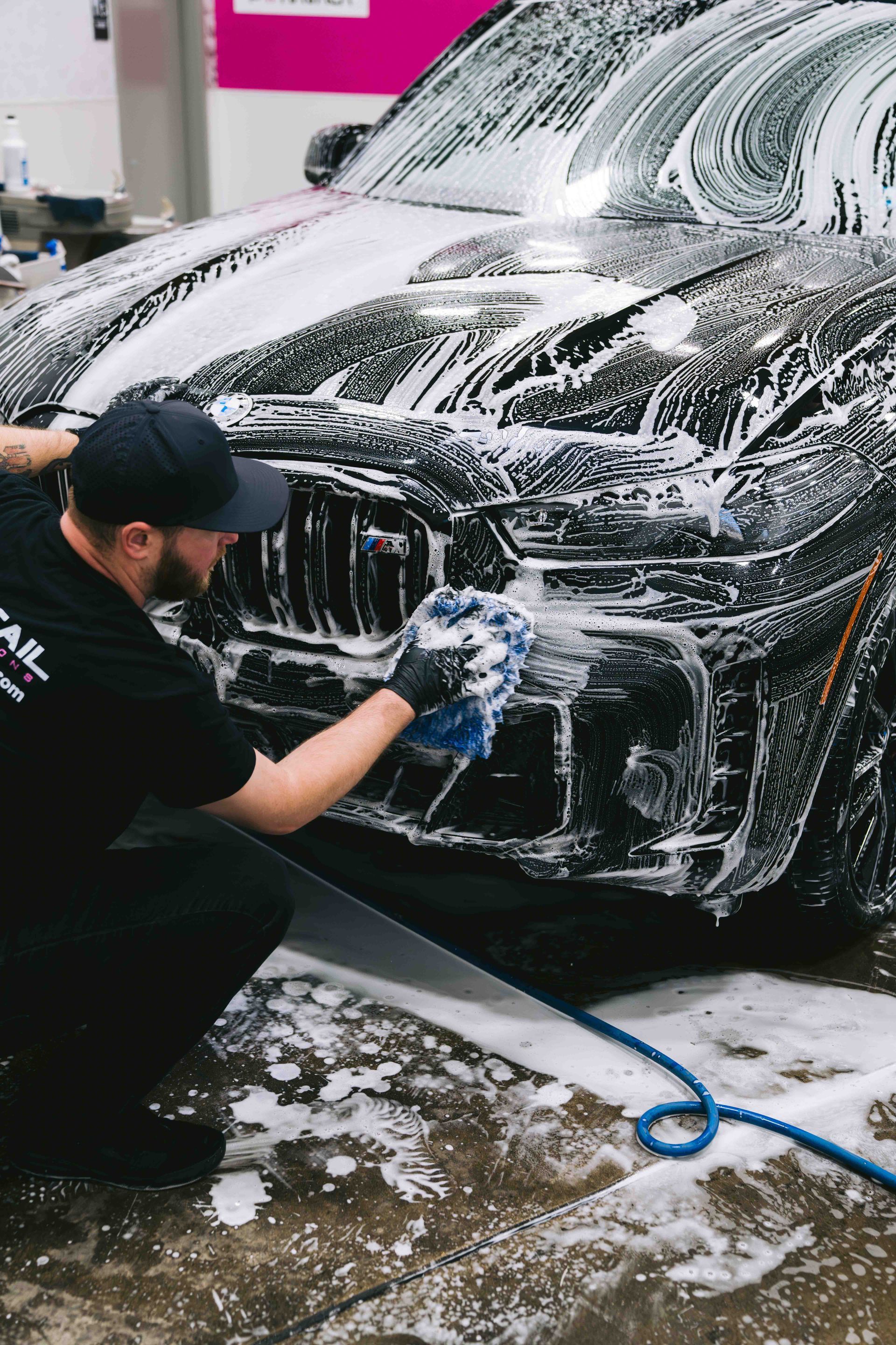 A man is kneeling down to wash a car with foam.