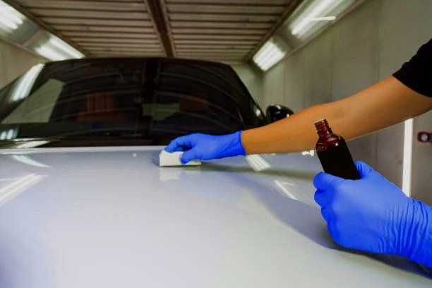 A person wearing blue gloves is polishing the hood of a car.