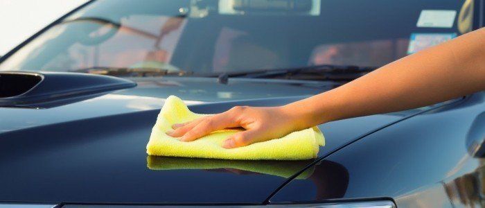 a person is cleaning the hood of a car with a yellow cloth .