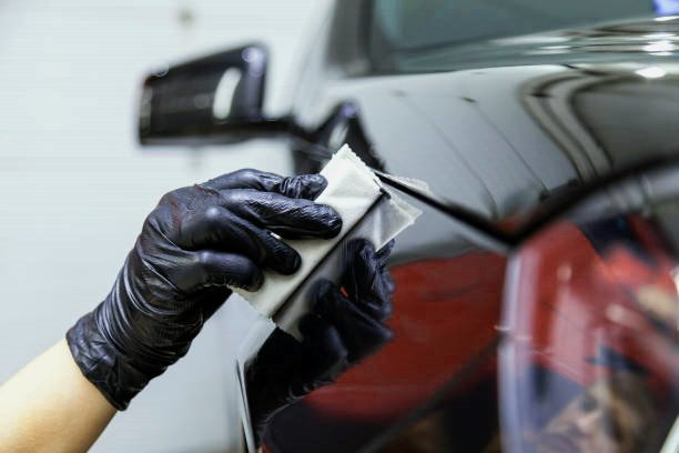 A person wearing black gloves is cleaning a car with a cloth.