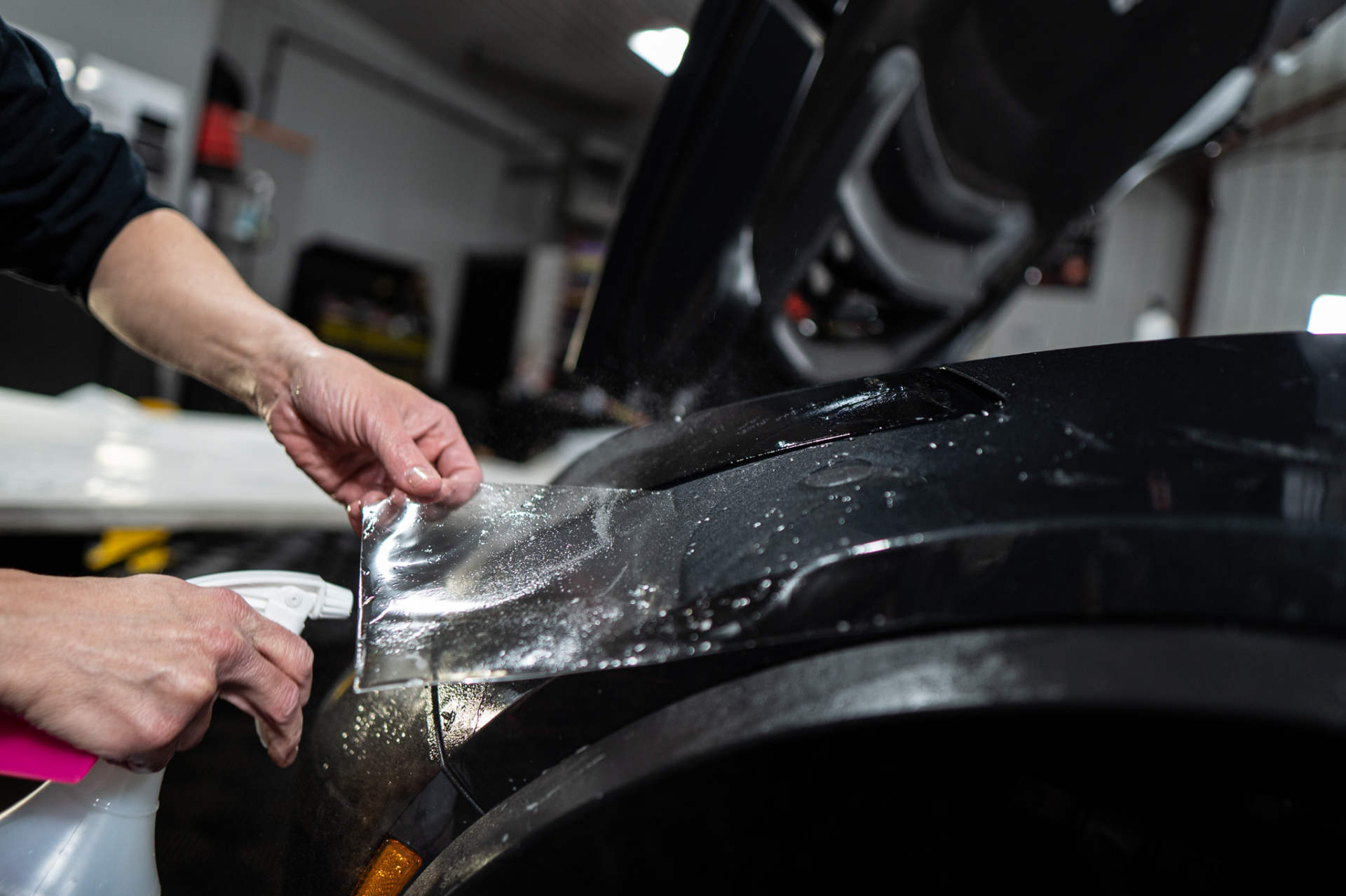 A person is applying a protective film to the fender of a car.