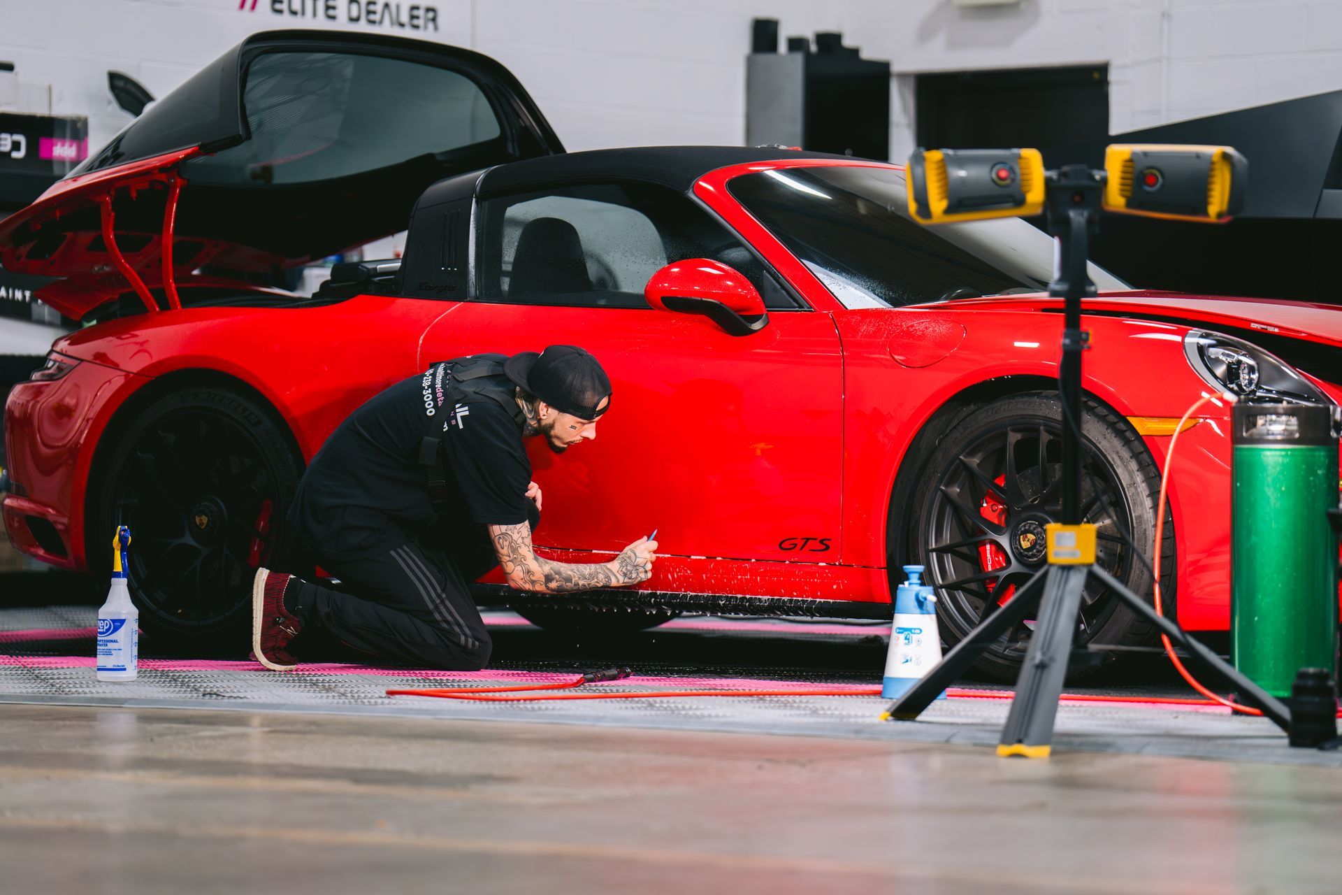Mechanic crouches beside a red sports car in a garage, using tools during maintenance.
